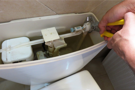 A person repairs the toilet tank with pliers, likely a plumbing issue.