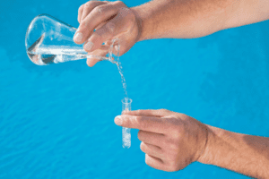 A pair of hands carefully pours liquid from a clear beaker into a test tube