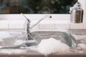 Kitchen sink overflowing with soapy water from a backed-up drain