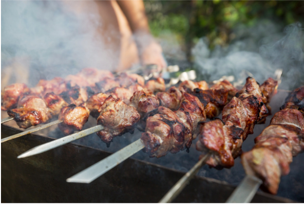 Meat skewers are displayed on a grill, smoke rising from the juicy chunks.