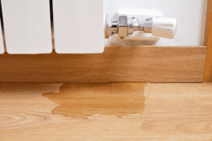 A leaking radiator has created a small puddle on the wooden floor