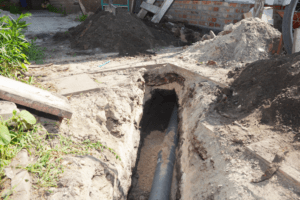 A newly-dug trench showcases a section of gray pipe laid within.