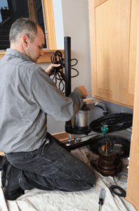 A plumber kneels, inspecting a sewage ejector pump in a home