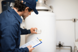 An HVAC technician in a blue uniform is inspecting a water heater