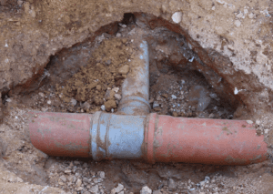 A buried terracotta pipe with a gray T-fitting is exposed in a trench